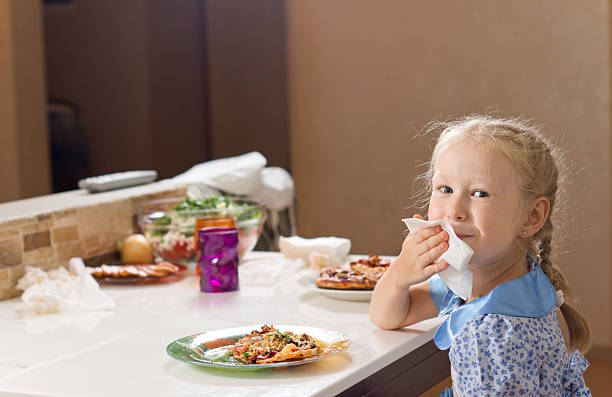 Beautiful blond girl wiping her mouth on a napkin Beautiful little blond girl wiping her mouth on a napkin as she sits at the table enjoying a large plate of homemade Italian pizza social grace stock pictures, royalty-free photos & images