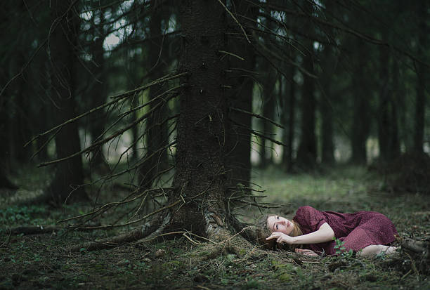 Young woman lies under on the moos under the tree. She looks up into the sky.