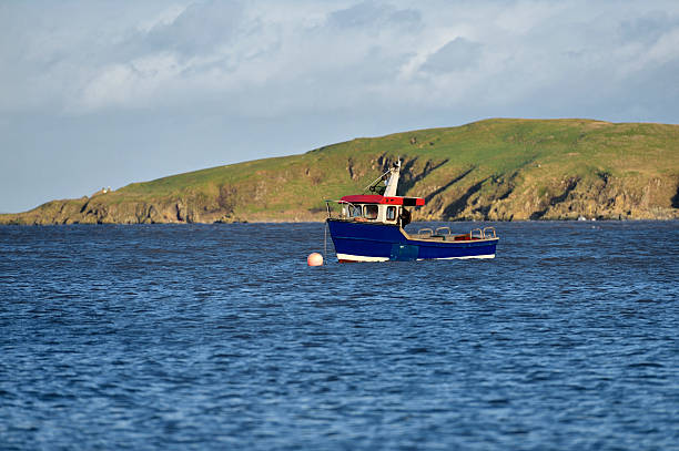 A small Scottish lobster boat moored in a bay in Dumfries and Galloway, south west Scotland. An island can be seen in the background.