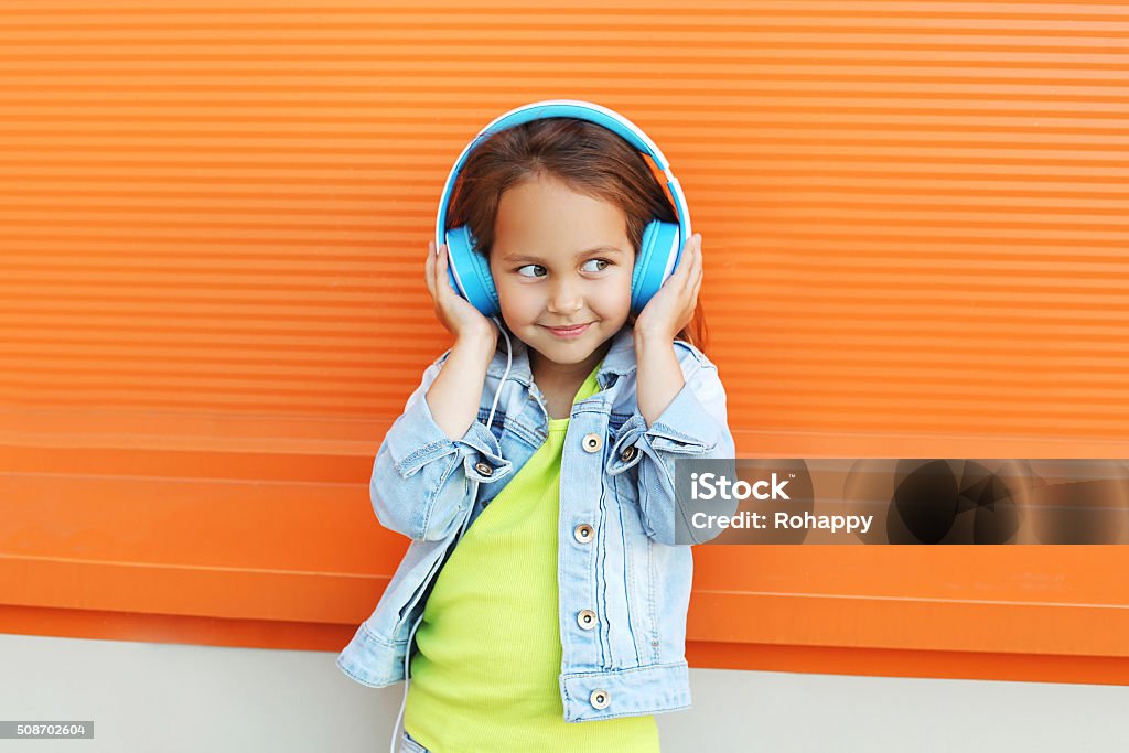 Happy child enjoys listens to music in headphones over orange Happy child enjoys listens to music in headphones over orange background Child Stock Photo