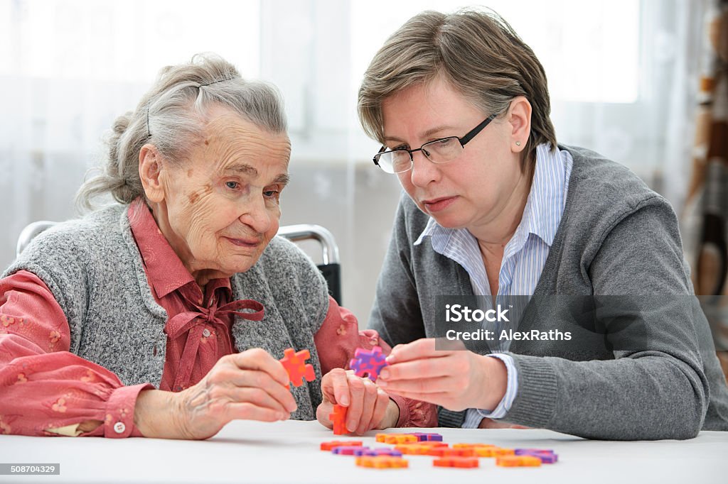 Senior woman with her elder care nurse Elder care nurse playing jigsaw puzzle with senior woman in nursing home Dementia Stock Photo