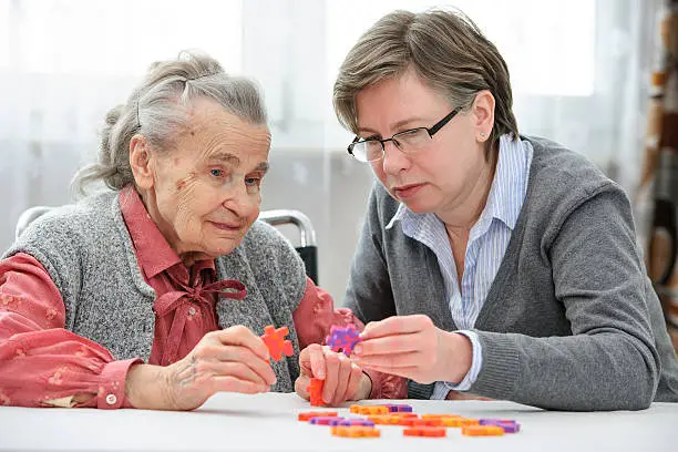 Elder care nurse playing jigsaw puzzle with senior woman in nursing home