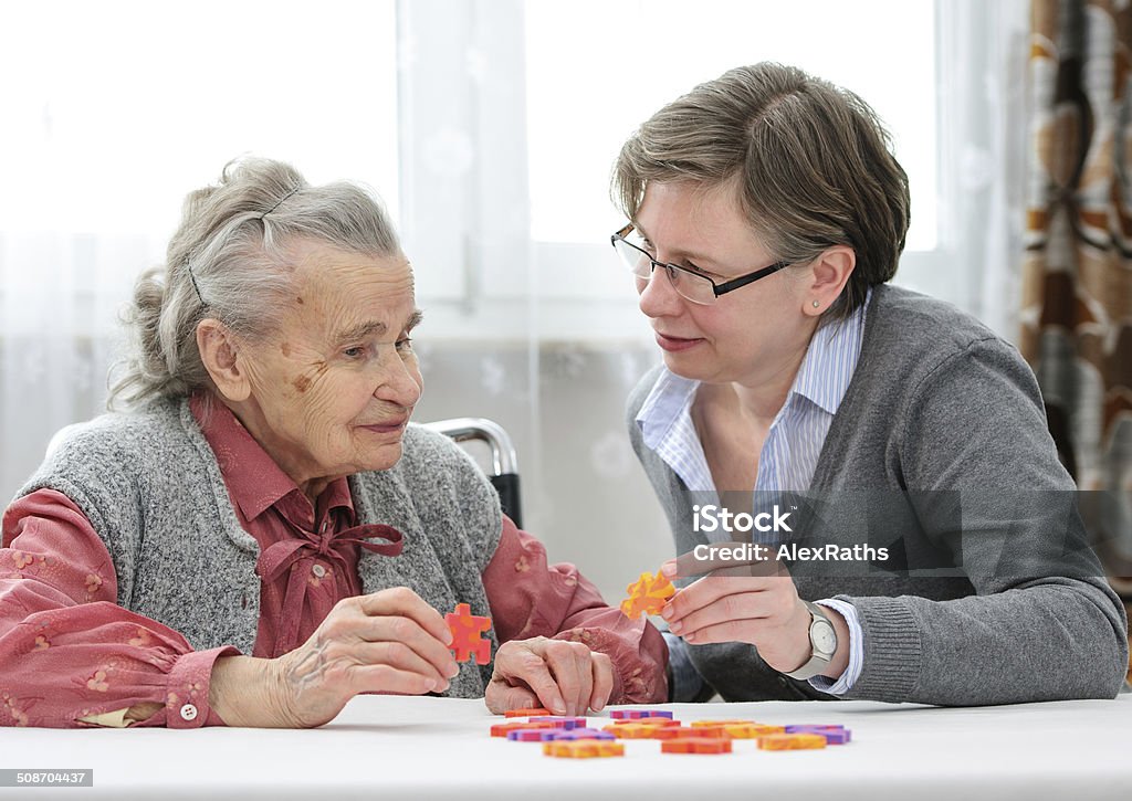 Senior woman with her elder care nurse Elder care nurse playing jigsaw puzzle with senior woman in nursing home Dementia Stock Photo