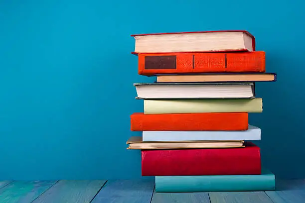 Stack of colorful books, grungy blue background, free copy space Vintage old hardback books on wooden shelf on the deck table, no labels, blank spine. Back to school. Education background