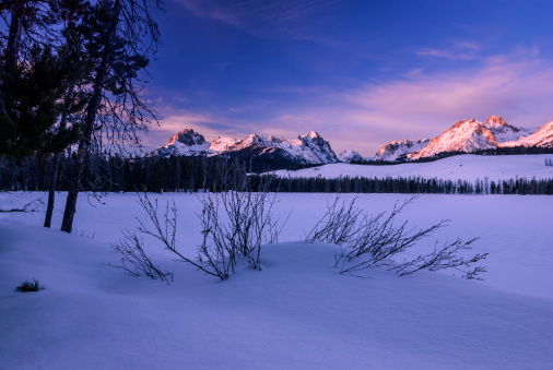 Beautiful sunrise in Stanley, Idaho on a fine winter morning with Sawtooth mountain range in the background and fresh snow in the foreground as seen from Little Redfish Lake