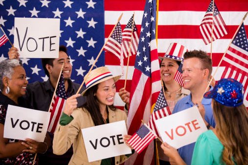 Multi-ethnic and mixed ages group excitedly encourage the public to vote during a political rally. American flags, voting signs.  Primary and presidential elections. 