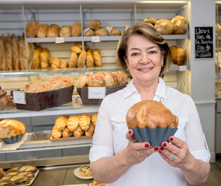Happy woman working at the bakery holding a freshly baked bread - small business concepts