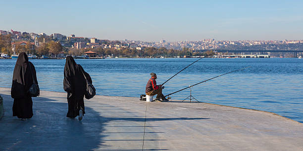 pescador en la sala de estar frente al mar paseo marítimo y musulmán vestido estimados a - headscarf islam senior adult east fotografías e imágenes de stock