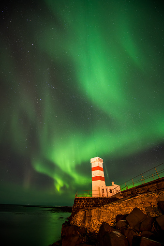 The spectacular natural phenomenon of a bright Aurora Borealis showing in the night skies of Winter above Gardur Lighthouse near Keflavik in Iceland
