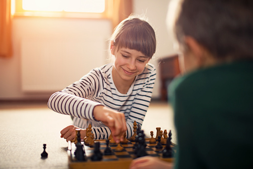 Little girl playing chess with her brother. Happy little girl aged 10 is making her move.