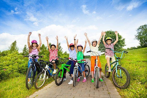 Excited kids in helmets sitting on their bikes with hands up in the air