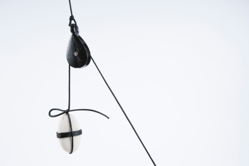 White stone, tied with dark rope, suspended with the use of a pulley. 