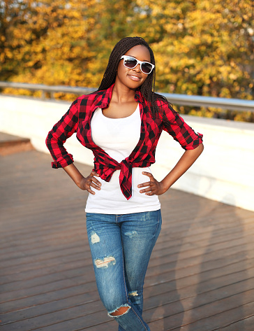 Beautiful young african woman wearing a sunglasses and red checkered shirt in city
