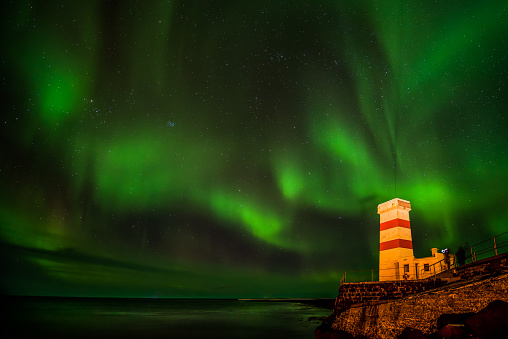 The spectacular natural phenomenon of a bright Aurora Borealis showing in the night skies of Winter above Gardur Lighthouse near Keflavik in Iceland