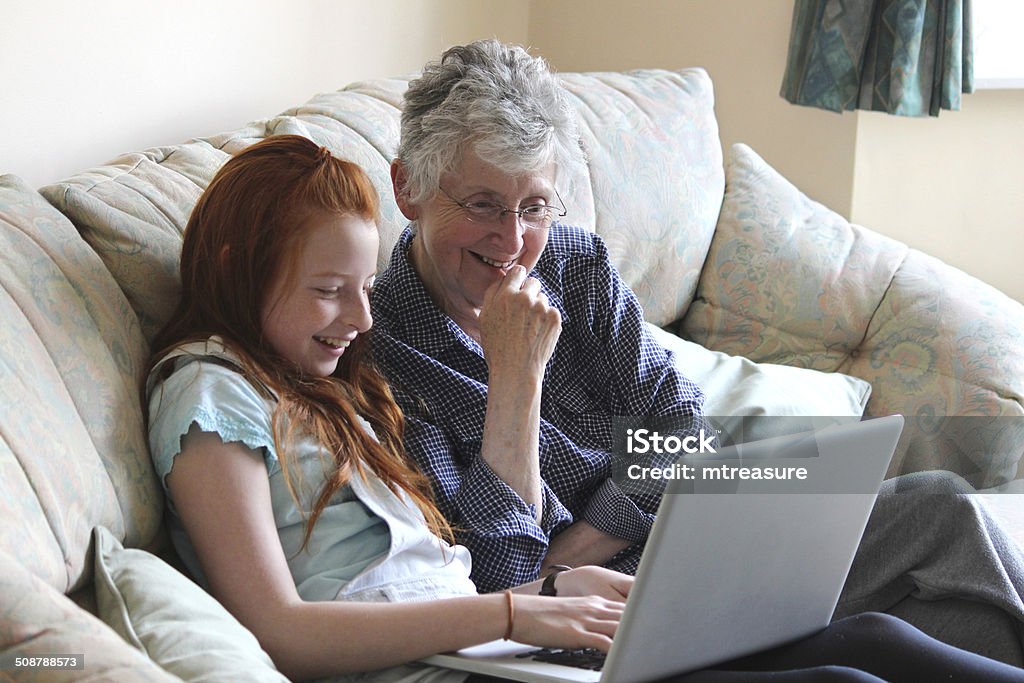 Image of girl showing grandmother how to use laptop computer Photo of a young girl showing her grandmother how to use a laptop computer.  They are pictured sat on the sofa together, laughing and smiling as they look at something funny and share the joke. Child Stock Photo