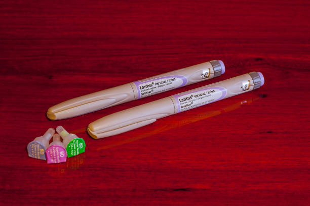 The Sanofi-aventis Lantus Glargine Insulin Pen Bogota, Colombia - February 04, 2016: The Lantus Glargine Insulin pen as distributed in Central and Latin America by Sanofi. The pen contains a built-in cartridge of Insulin that controls the blood glucose level for diabetic patients. To the left are three different sizes of needles that are sealed in individual containers; the one with the green label is the shortest at 4 mm of length. The purple at 5 mm, and the one with the pale blue label is the longest at 8 mm. The pen device is manufactured by Sanofi-Aventus in Germany. Photo shot in a studio environment, shows two pens, placed on a polished rosewood surface. Closeup shot; horizontal format. No people. lantus insulin stock pictures, royalty-free photos & images