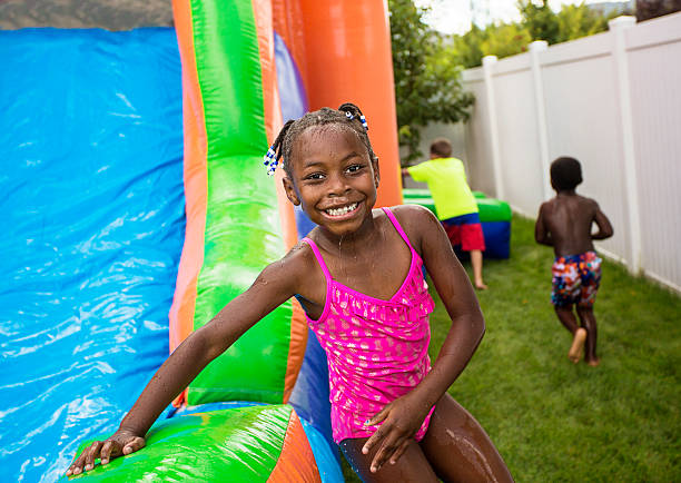 sorridente menina a brincar ao ar livre em um salto insufláveis casa - house bouncing multi colored outdoors imagens e fotografias de stock