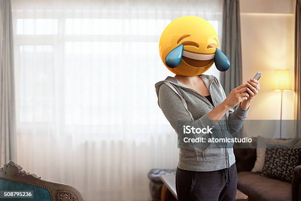 Mujer Usando Emoji Máscaras Mientras Observando A Su Teléfono Foto de stock y más banco de imágenes de Emoticono