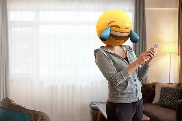 Woman wearing tears of joy emoji masks while looking at her phone. Image created by mix of photography and CGI.