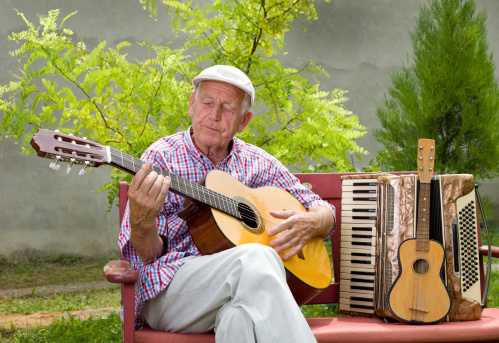 Old man playing acoustic guitar with closed eyes in his garden