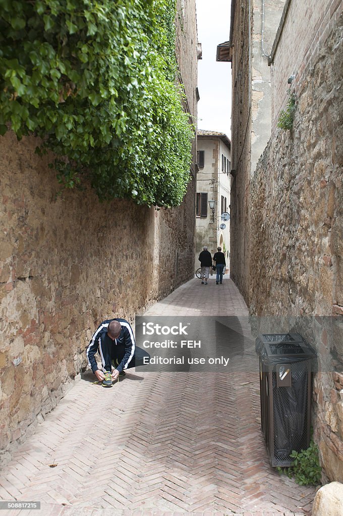 Narrow alley Montepulciano, Italy- May 19, 2014: A man tie his shoe in a narrow alley in the city og Montepulciano in Tuscany, Italy. Alley Stock Photo