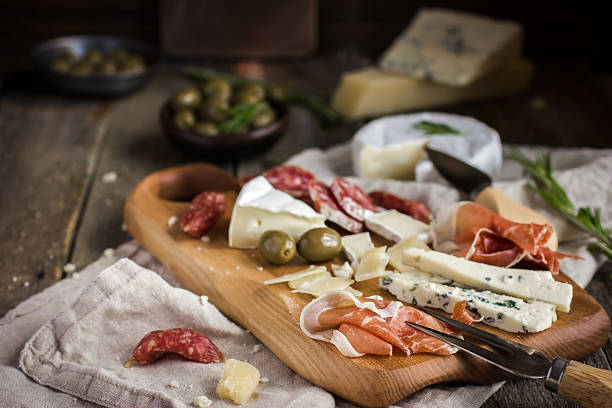 Appetizers. Various types of cheese, salami and prosciutto on w Appetizers. Various types of cheese, salami and prosciutto on wooden cutting board, rustic background prosciutto brie stock pictures, royalty-free photos & images
