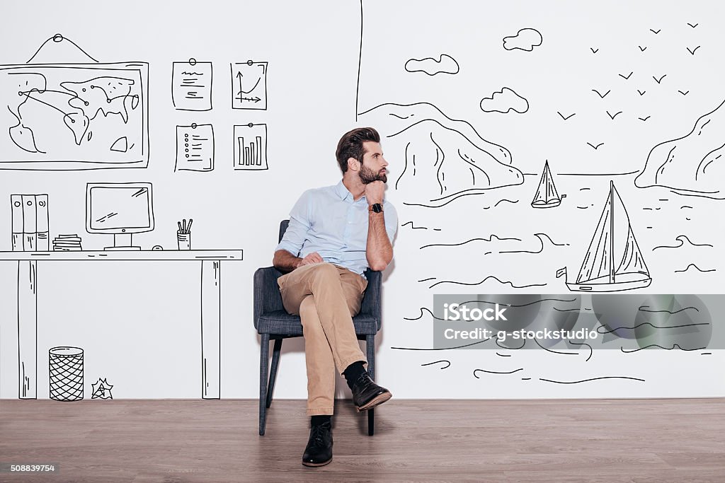 Your dreams can send you far away. Young handsome man keeping hand on chin and looking away while sitting in the chair against illustration of fjord vs. working place Day Dreaming Stock Photo