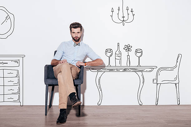 Table for two. Young handsome man keeping legs crossed and looking at camera while sitting in the chair against illustration of dining table in the background chandelier photos stock pictures, royalty-free photos & images