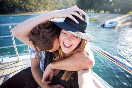 Young couple on Pittwater ferry taking selfie and laughing as he kisses her neck on a sunny summer day