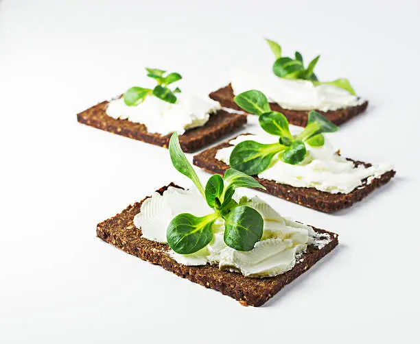 Rye loaves sandwich with fresh cornsalad on white table.