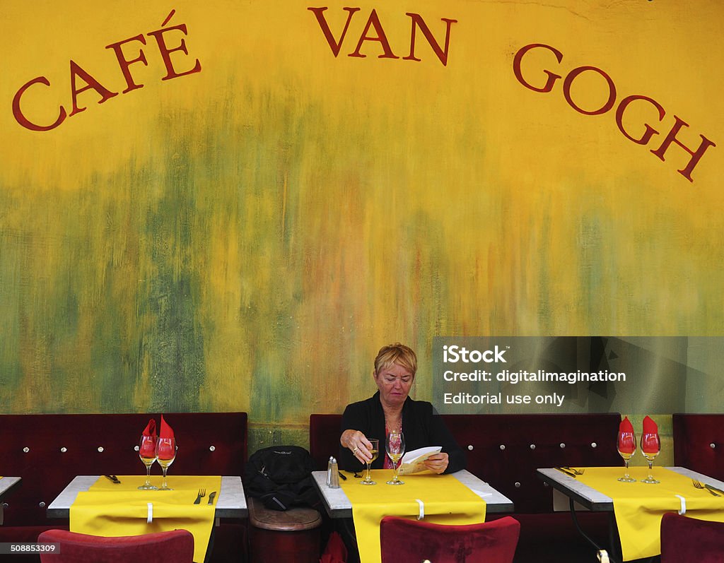 Café van Gogh, Arles Arles, France - July 10, 2014: Woman is taking a refreshment at café van Gogh in the center of Arles in South France. This cafe is painted by the famous painter van Gogh and well knowned as "Cafe du Nuit". Picture is taken from  Place du Forum, a famous square in Arles, with a lot of restaurants. Cafe Stock Photo