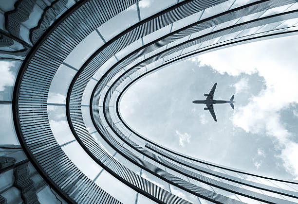Modern architecture building with landing airplane Low view blue colorized picture of modern architecture building with landing airplane in background planes flying overhead stock pictures, royalty-free photos & images