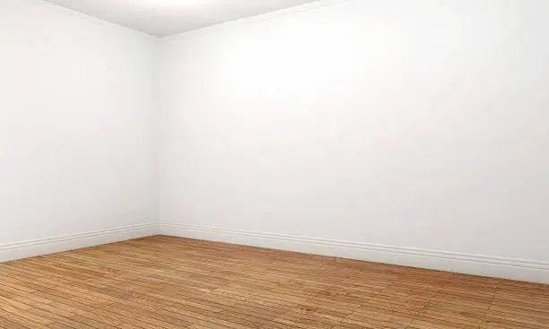 Empty apartment room with white walls and ceiling, and brown wooden parquet floor. Perspective view of an empty corner. Bright illumination with copy space.