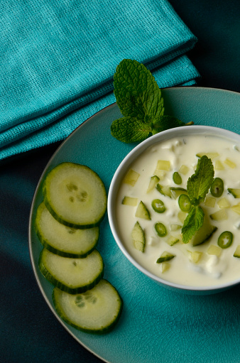 Restaurant side dish of fresh spicy cucumber and mint raita chutney, with slices of cucumber and a sprig of fresh mint