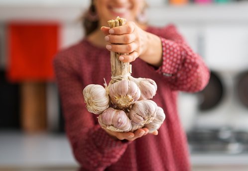 A bunch of heads of garlic are tied together. Smiling, a woman in the background holds them up.