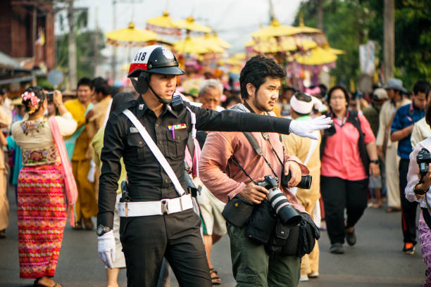 Mae Hong Son, Thailand - April 8, 2014: Police direct pedestrians as families take part in the Poi Sang Long festival. This is an annual event when young boys who will enter the temple as novice monks are dressed in bright coloured costumes and make up and paraded around on the shoulders of male family members. The festival takes place in many places in the north of Thailand. This event was held in Mae Hong Son, Thailand, Asia.