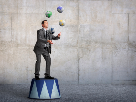 A businessman standing on a pedestal juggling globes showing different parts of the world.