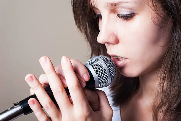 Girl singing with microphone on gray background