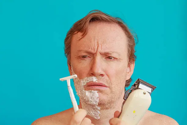 a man with shaving -foam about to shave but is undecided whether to choose razor or razor-blade