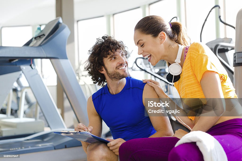 Woman with personal trainer in the gym. Female talking with personal trainer in the gym. Female smiling and looking plan in intsructor's hands. 20-29 Years Stock Photo