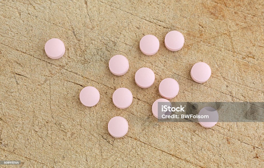 Famotidine tablets on a wood cutting board Top view of a group of famotidine tablets on an old cutting board illuminated with natural light. Brown Stock Photo