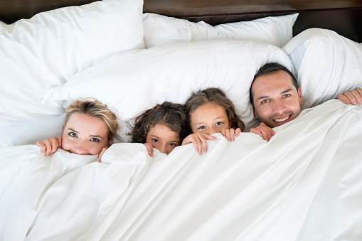 Happy Latin American family in bed under the covers looking playful - lifestyle concepts