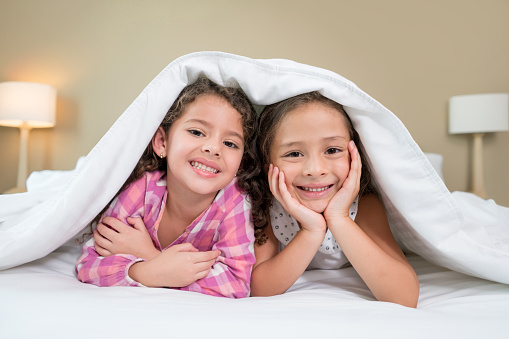 Beautiful little girls in bed under the covers looking at the camera smiling