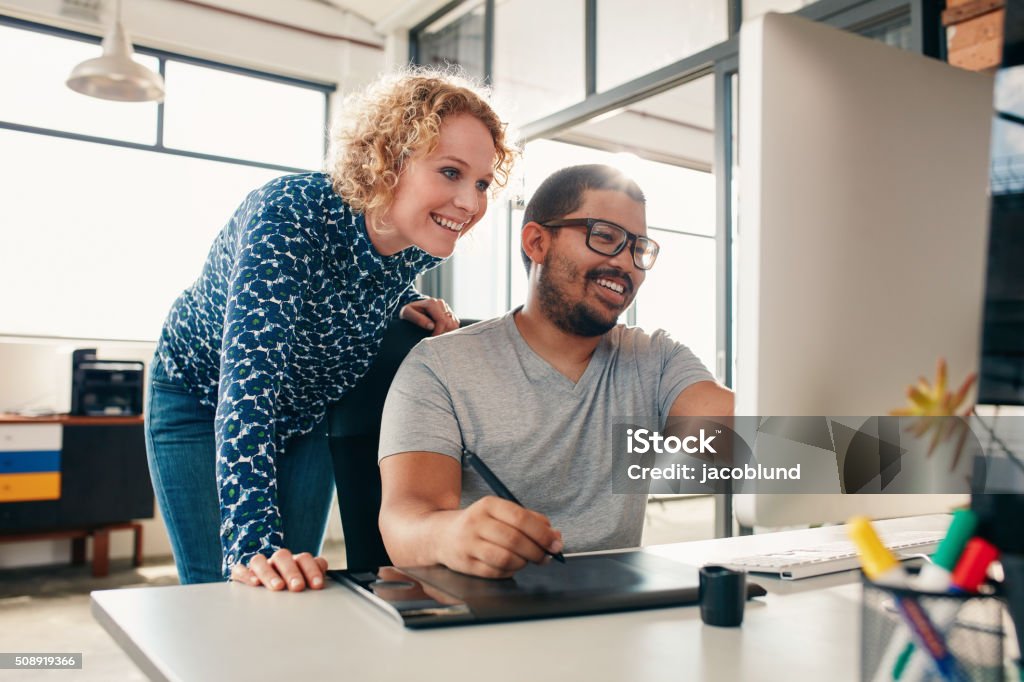 Creative people coworking on a new project Two young male and female designers working together, with man editing artwork using graphics tablet and a stylus. Creative people coworking on a new project in office. Graphic Designer Stock Photo