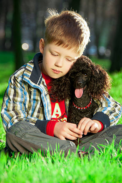 istock Boy sitting on the grass with a black poodle 508919750