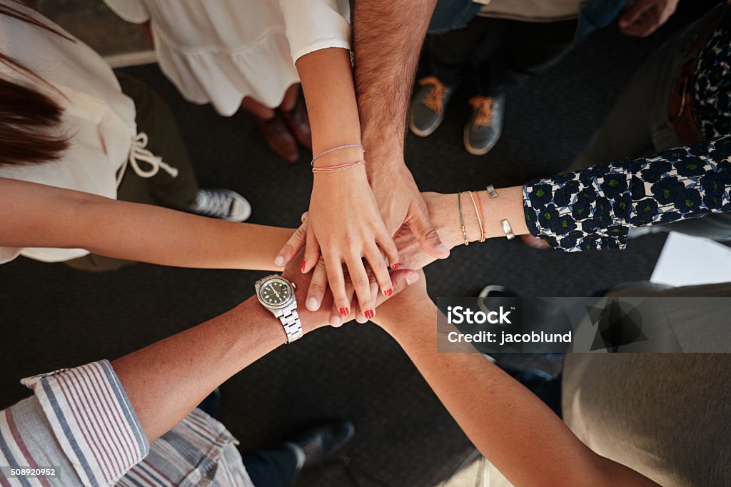 Symbol of teamwork, cooperation and unity Top view of young creative professionals putting their hands together as a symbol of teamwork, cooperation and unity. Stack of hands of men and woman. Stacked Hands Stock Photo