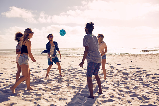 Portrait of group of happy friends having fun on the beach and playing with ball on a summer day.