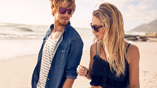 Closeup portrait of young couple talking while walking along a beach. Young man and woman strolling on a beach.