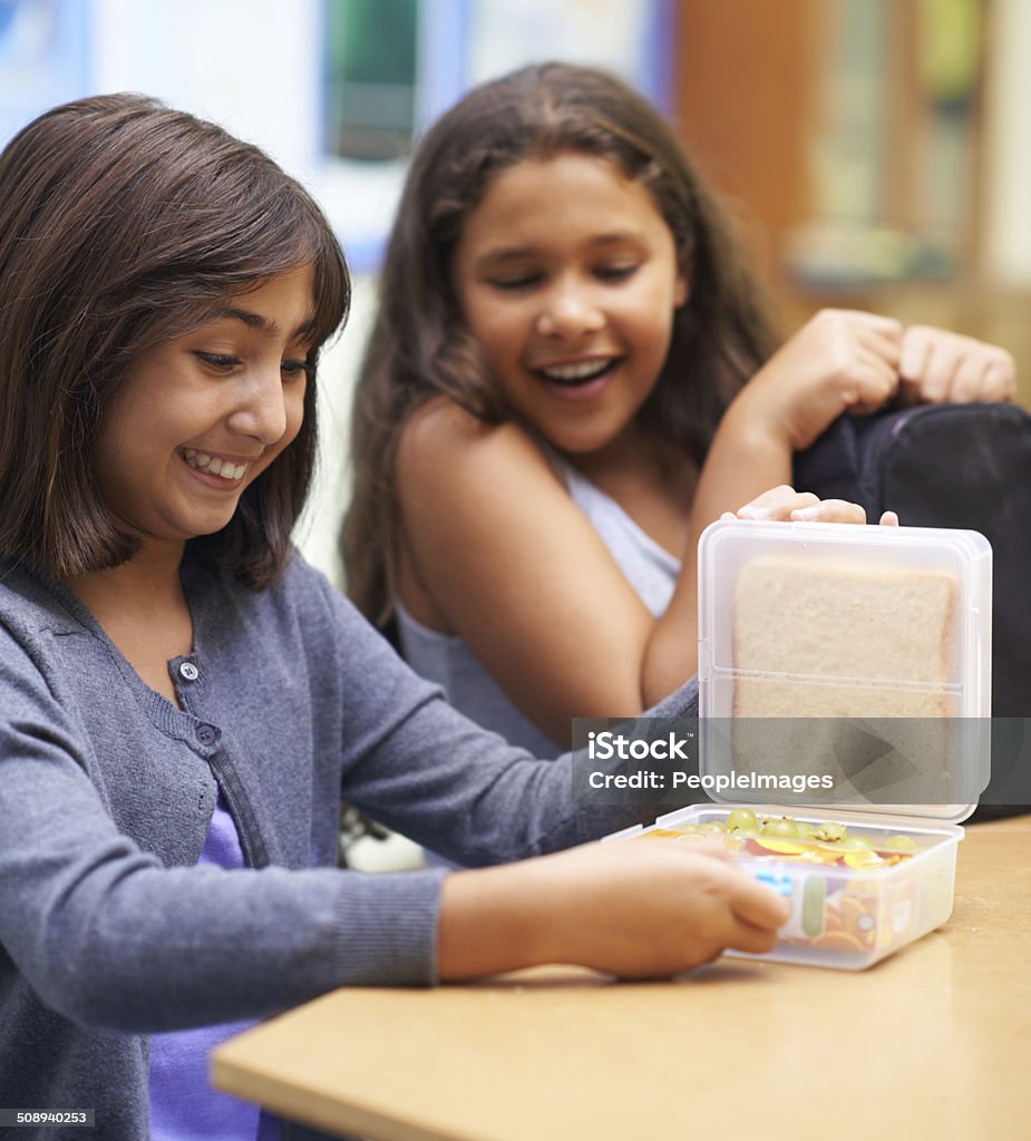 Opening her lunch in the cafeteria Two young school girls sitting in the cafeteria during lunchtime Lunch Box Stock Photo