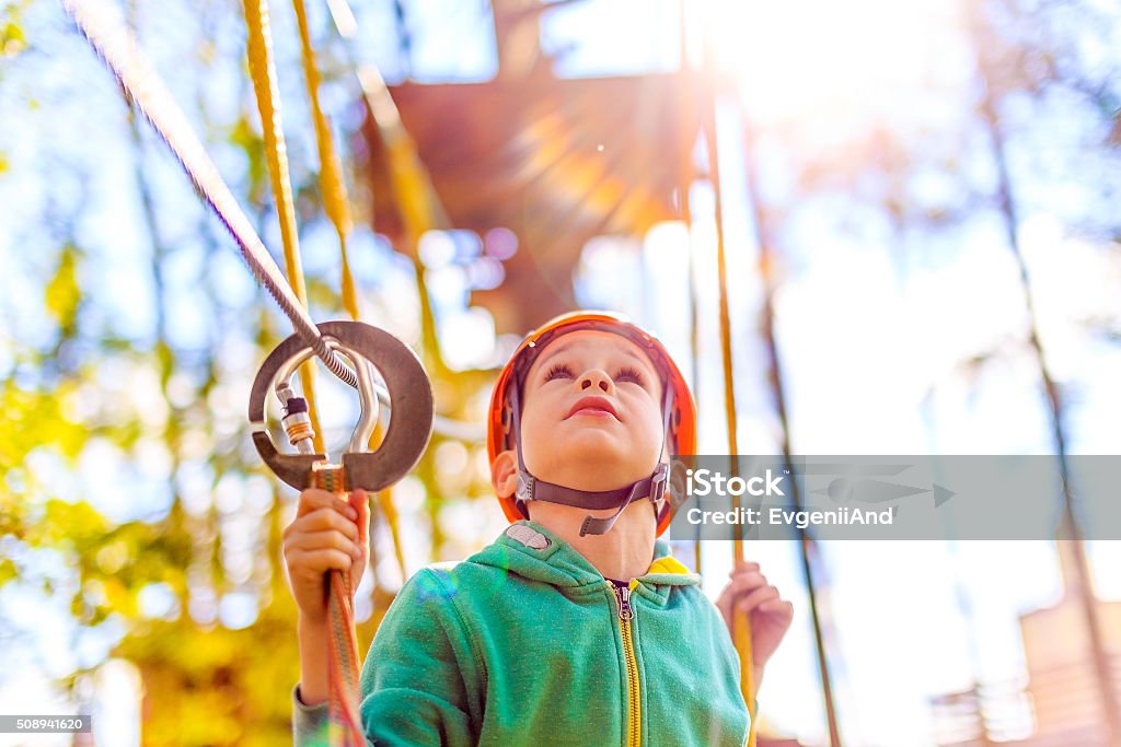 boy in the rope park looking up rope course at a summer camp. child wearing a helmet on the obstacle course. blurred background and blurred motion due to the concept Child Stock Photo